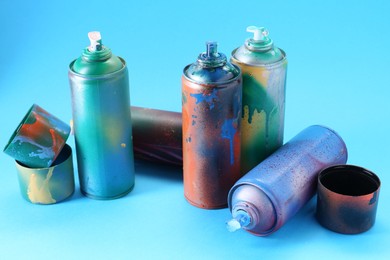 Photo of Many spray paint cans and caps on light blue background