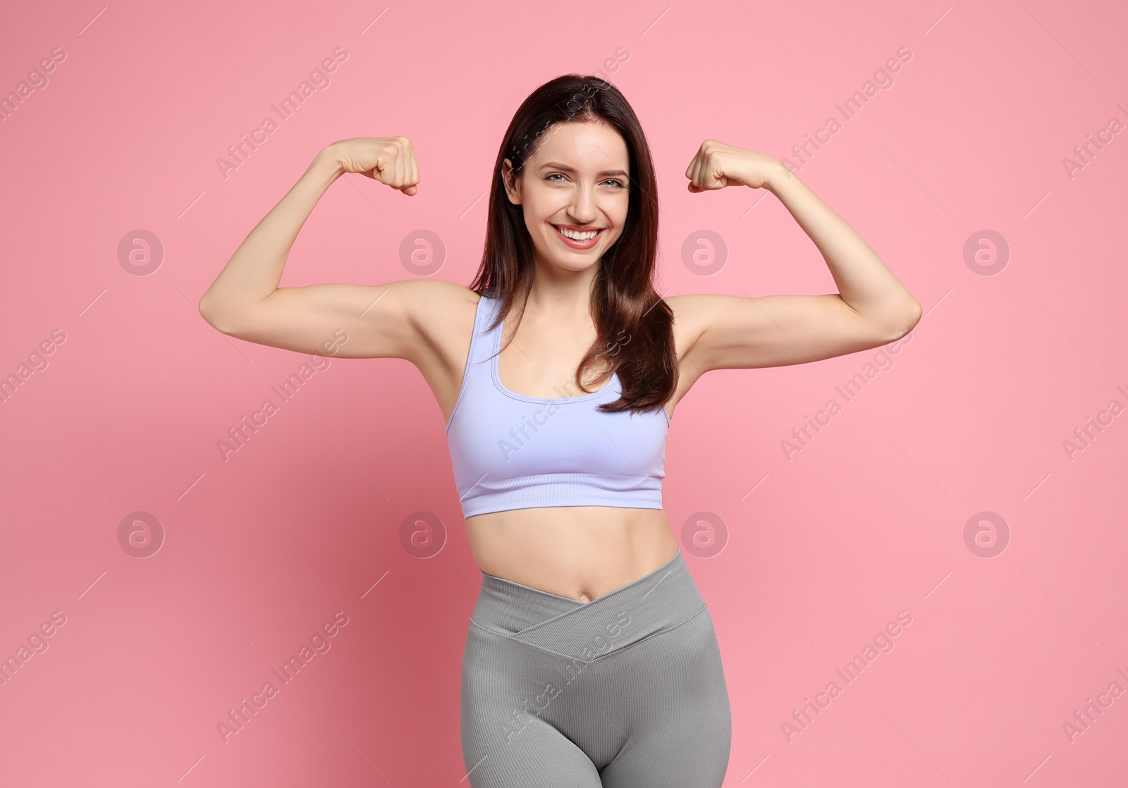 Photo of Happy young woman with slim body showing her muscles on pink background