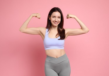 Photo of Happy young woman with slim body showing her muscles on pink background