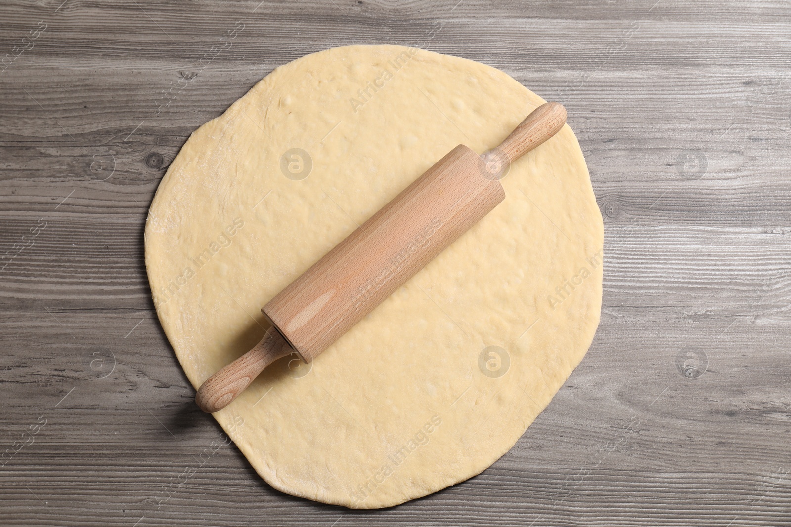 Photo of Raw dough and rolling pin on wooden table, top view