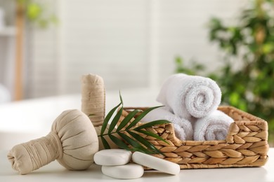 Spa composition. Towels, stones, herbal bags and palm leaves on white table indoors