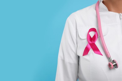 Photo of Doctor with pink ribbon and stethoscope on light blue background, closeup and space for text. Breast cancer awareness