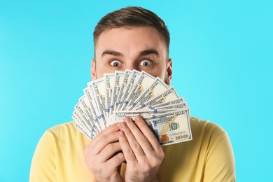 Emotional young man with money on color background