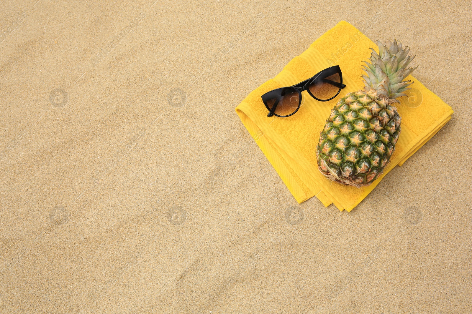 Photo of Fresh pineapple, sunglasses and towel on sand, top view. Space for text