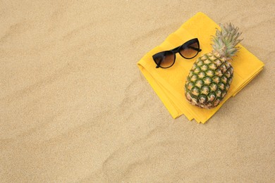 Photo of Fresh pineapple, sunglasses and towel on sand, top view. Space for text