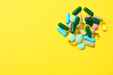 Photo of Different vitamin pills on yellow background, top view. Space for text