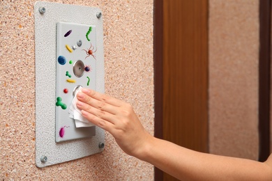 Woman using tissue paper to press elevator call button full of microbes, closeup