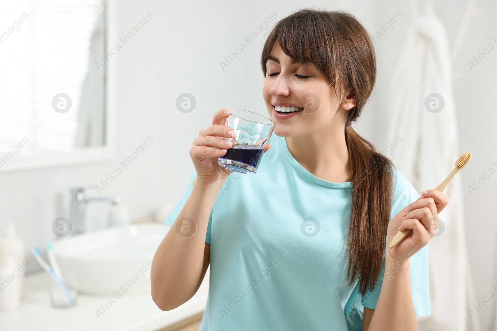 Photo of Young woman using mouthwash in bathroom. Oral hygiene