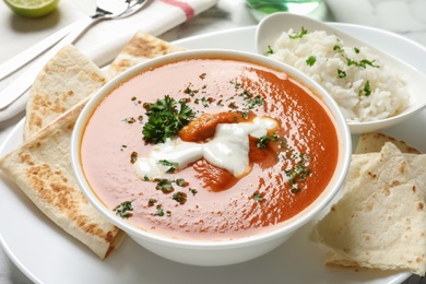 Photo of Delicious butter chicken in bowl served with rice on dish. Traditional Murgh Makhani dish