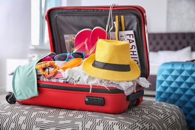 Photo of Open suitcase with different clothes and accessories for summer journey on ottoman chair