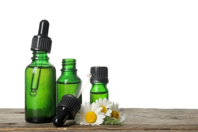 Photo of Chamomile flowers and cosmetic bottles of essential oil on wooden table against white background. Space for text