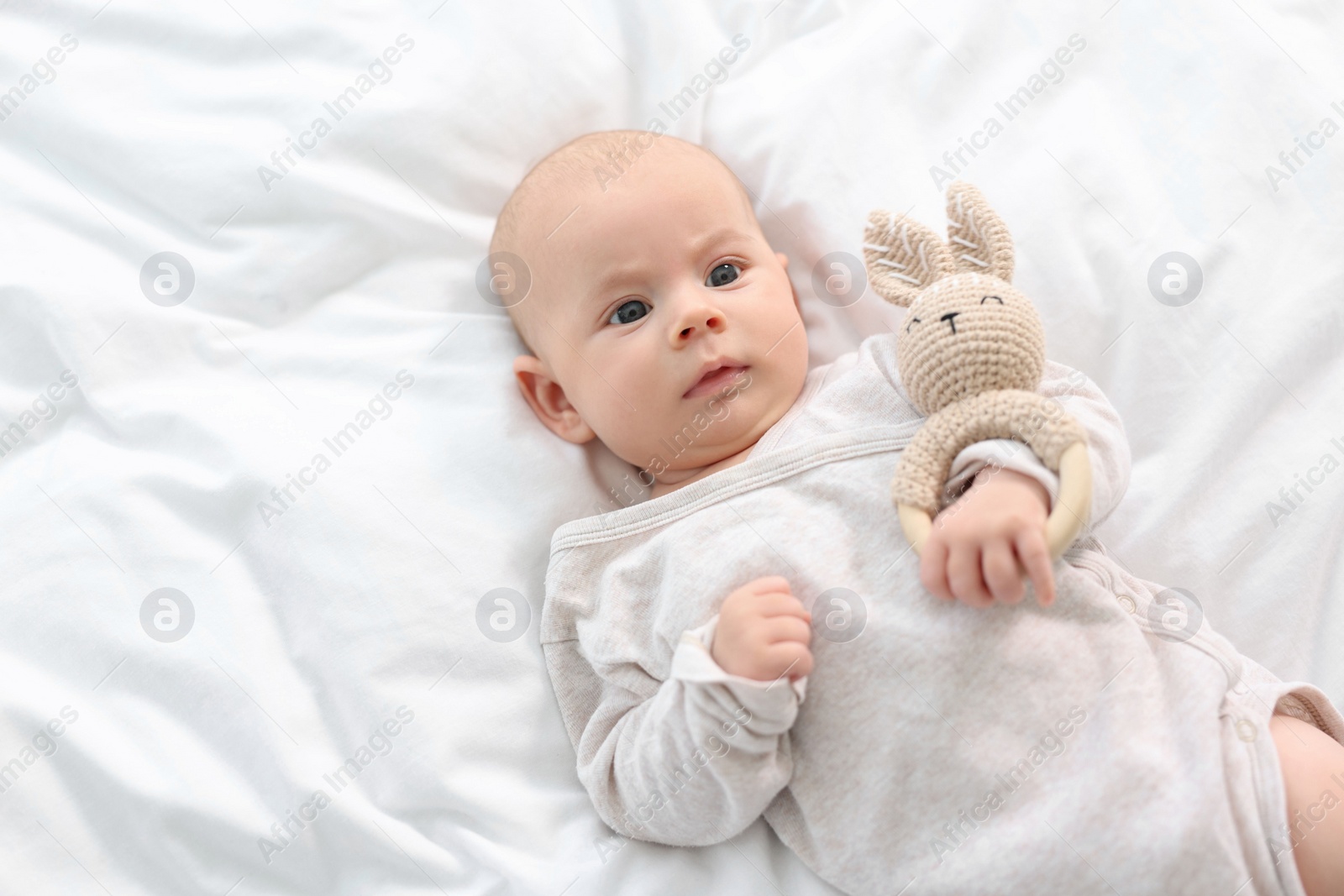 Photo of Cute little baby with toy lying on white sheets, top view. Space for text