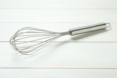 Photo of Metal whisk on white wooden table, closeup