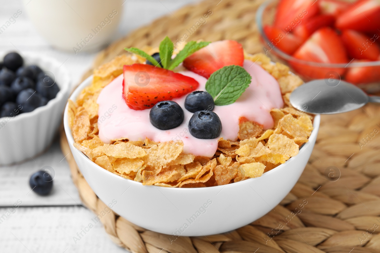 Photo of Delicious crispy cornflakes, yogurt and fresh berries in bowl on white table, closeup. Healthy breakfast