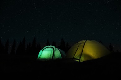 Photo of Camping tents glowing at night outdoors. Space for text
