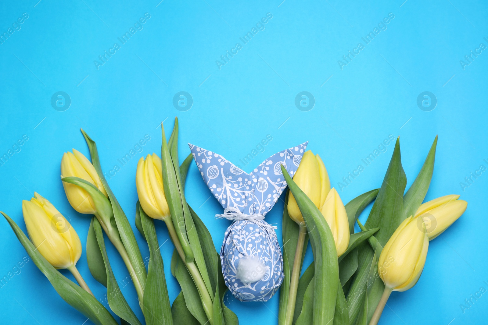 Photo of Easter bunny made of paper and egg among beautiful tulips on light blue background, flat lay