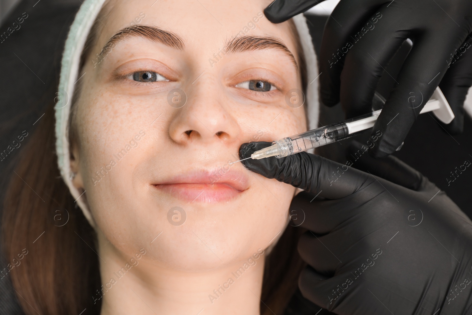 Photo of Cosmetologist giving lips injection to patient, closeup. Cosmetic surgery