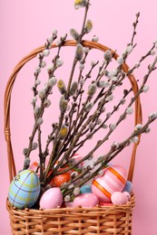 Photo of Wicker basket with beautiful willow branches and painted eggs on pink background. Easter decor