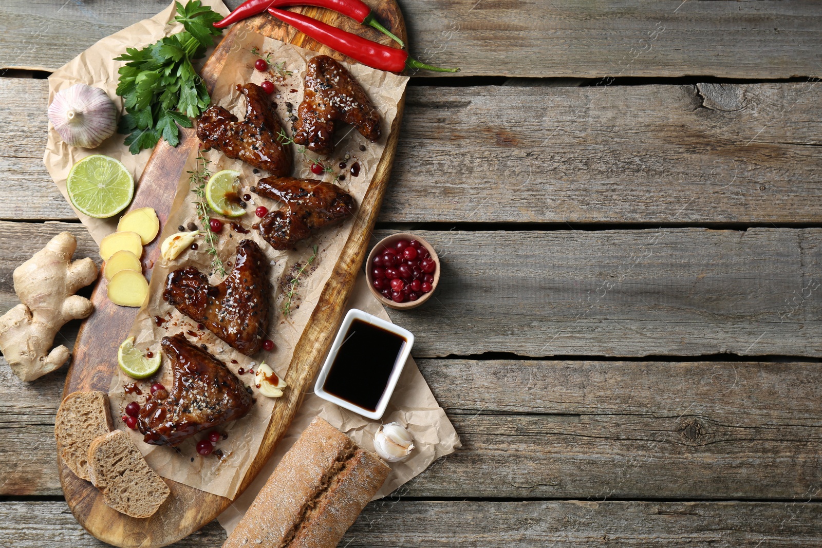 Photo of Tasty chicken wings glazed in soy sauce with garnish on wooden table, flat lay. Space for text