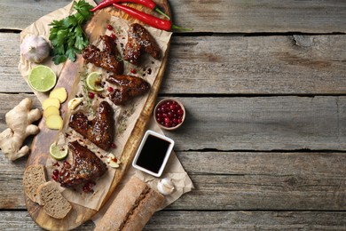 Tasty chicken wings glazed in soy sauce with garnish on wooden table, flat lay. Space for text