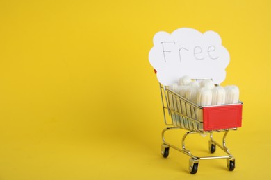 Tampons and card with word Free in small shopping cart on yellow background. Space for text