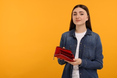 Photo of Sad woman showing empty wallet on orange background, space for text
