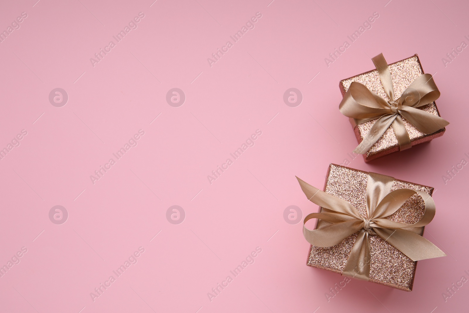 Photo of Shiny gift boxes with golden bows on pink background, flat lay. Space for text