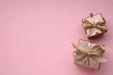 Shiny gift boxes with golden bows on pink background, flat lay. Space for text