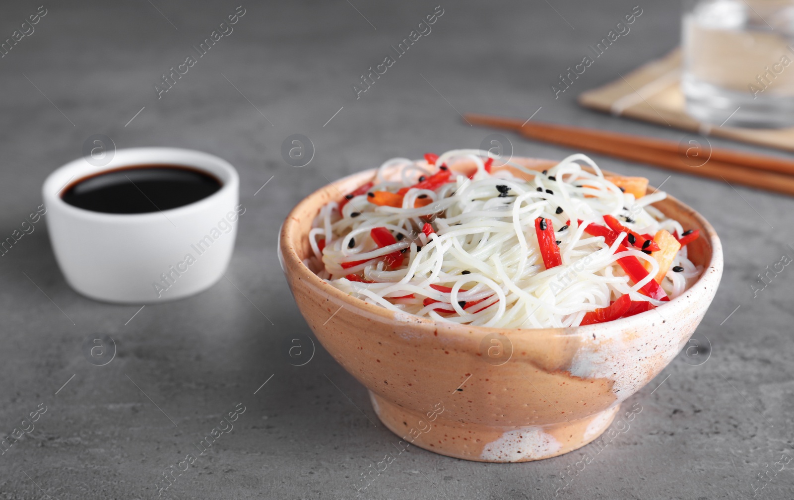 Photo of Bowl of noodles with vegetables and soy sauce on table