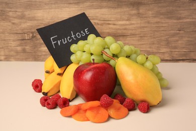 Photo of Card with word Fructose, delicious ripe fruits, raspberries and dried apricots on beige table
