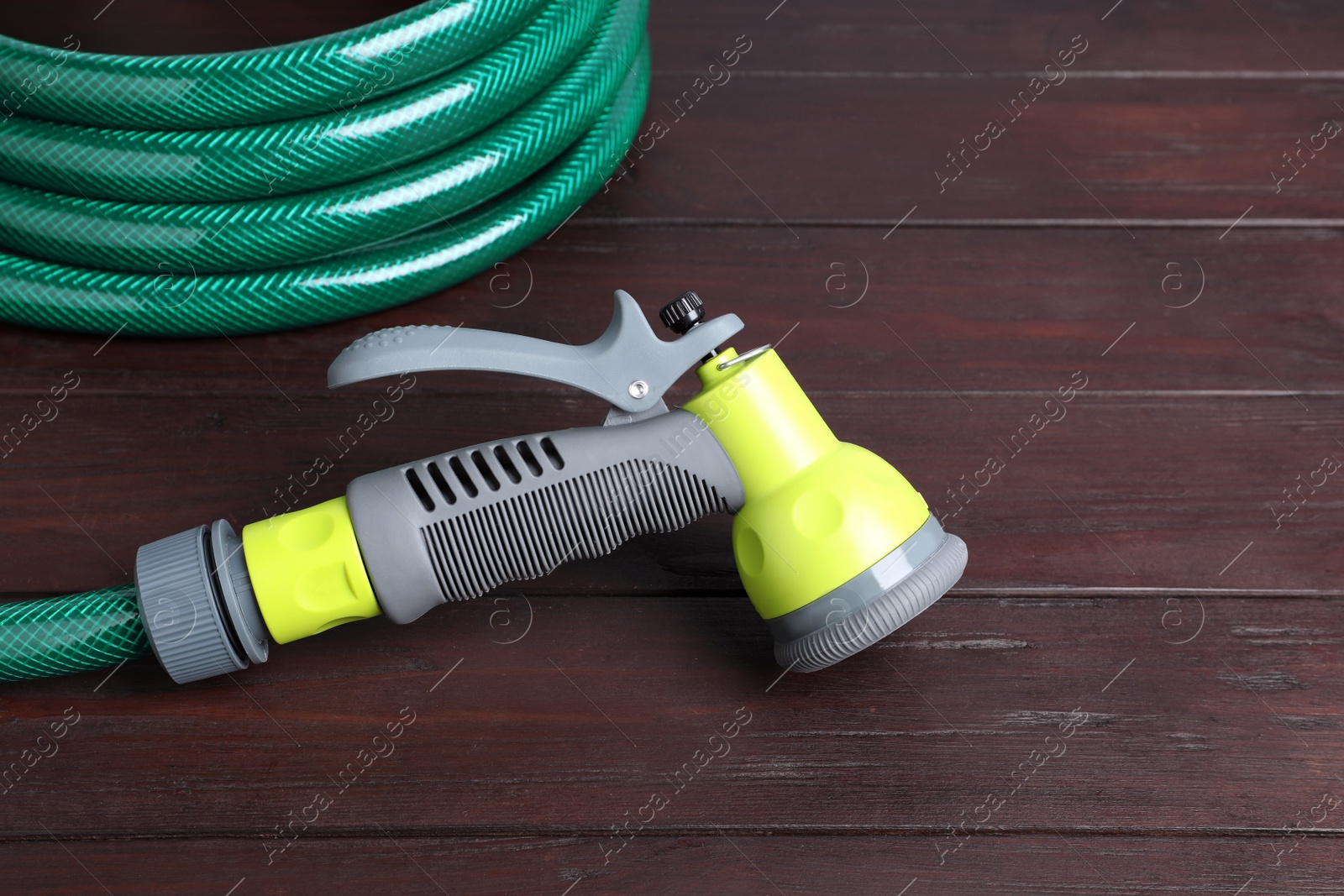 Photo of Green garden hose with spray gun on wooden table