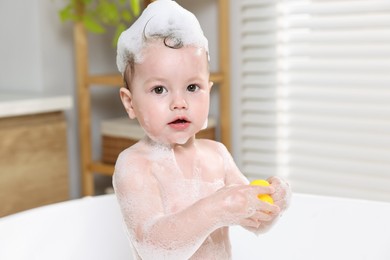 Cute little child playing with toy duck in bathtub at home