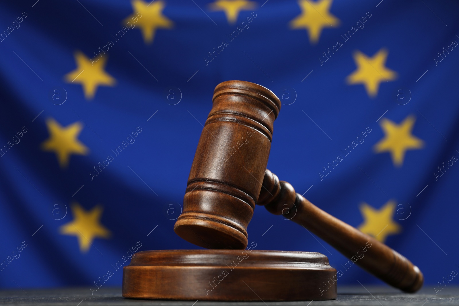 Photo of Wooden judge's gavel on black table against flag of European Union, closeup