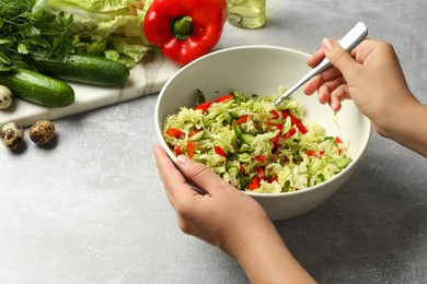 Photo of Woman making tasty salad with Chinese cabbage at light grey table, closeup