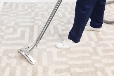 Photo of Male worker removing dirt from carpet with professional vacuum cleaner indoors