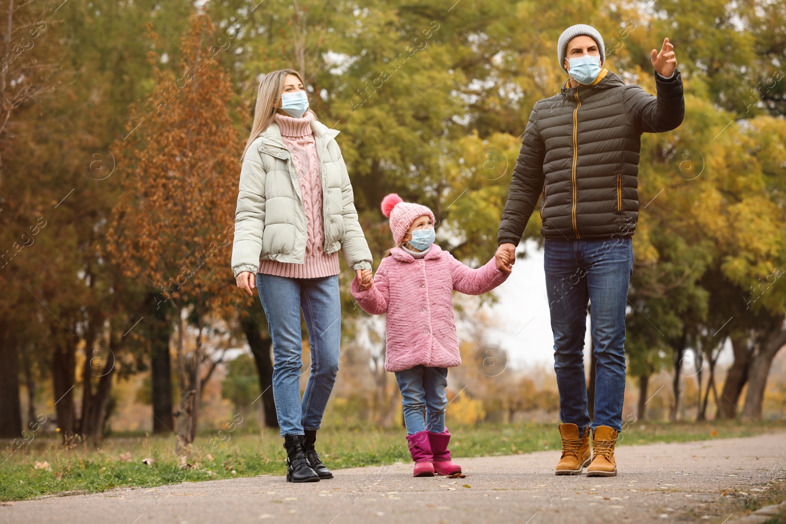 Photo of Family in medical masks walking outdoors on autumn day. Protective measures during coronavirus quarantine