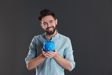 Photo of Happy young man with piggy bank and space for text on grey background. Money saving