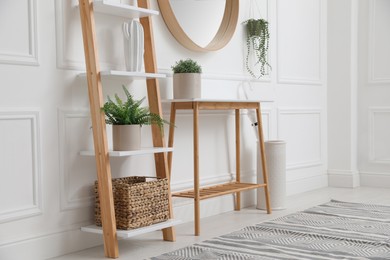 Photo of Console table with shelving unit and mirror on white wall in hallway. Interior design