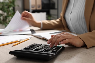 Woman using calculator while working with document at wooden table, closeup