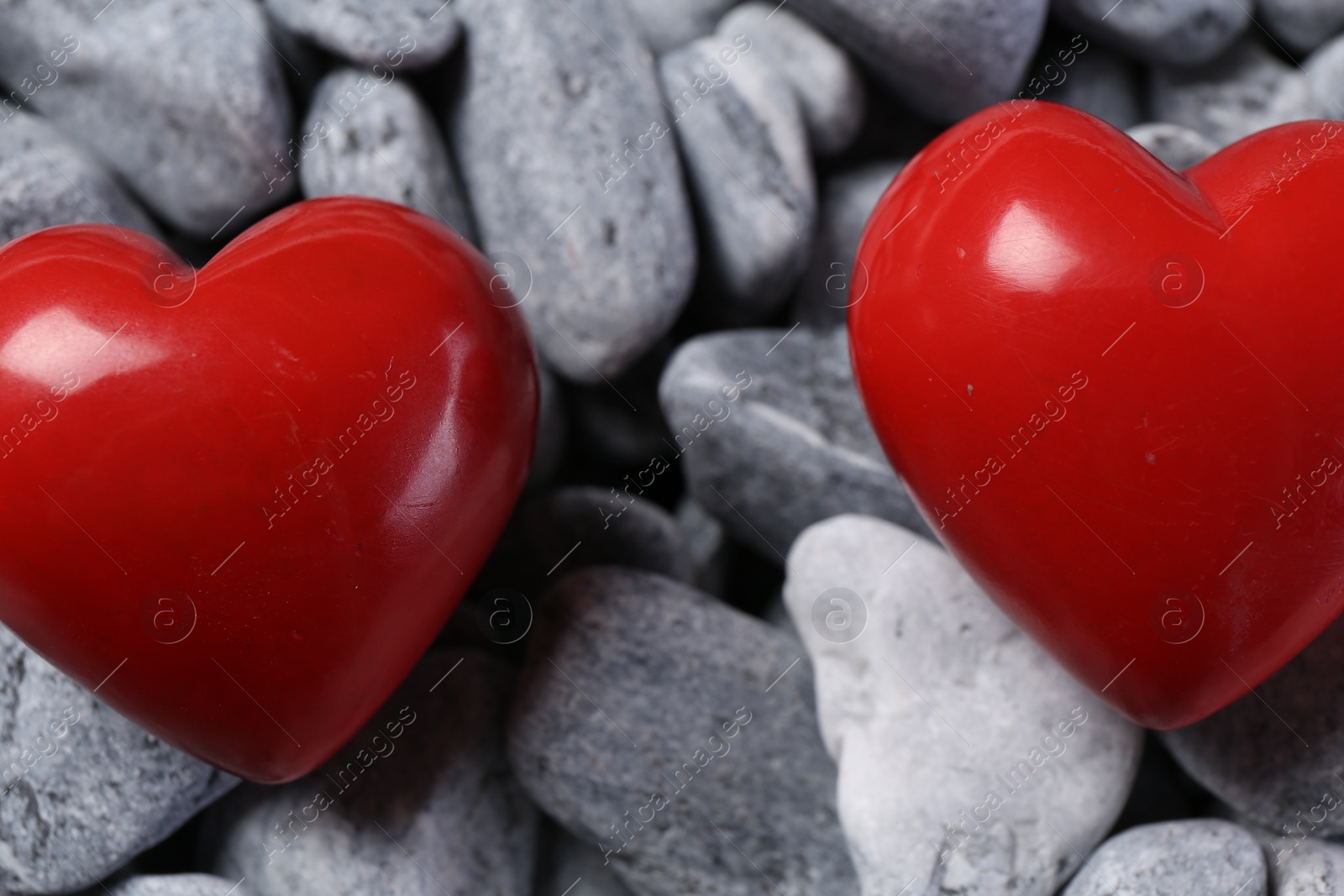 Photo of Red decorative hearts on grey stones, closeup