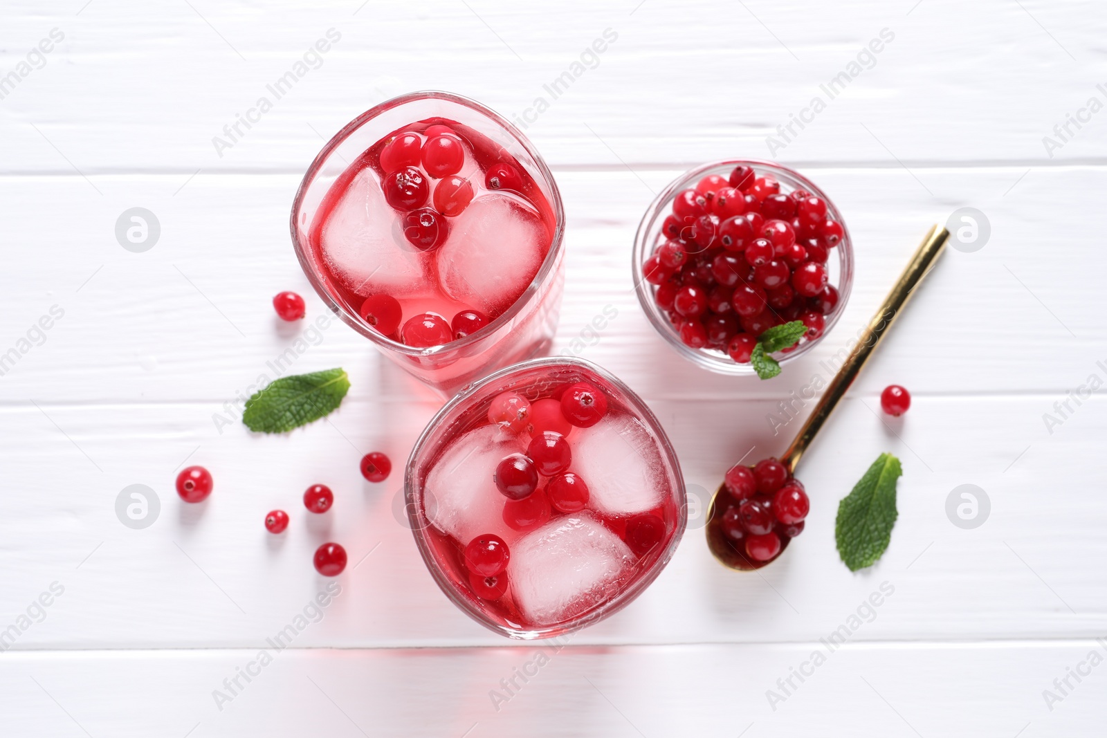 Photo of Tasty cranberry juice with ice cubes in glasses and fresh berries on white wooden table, flat lay