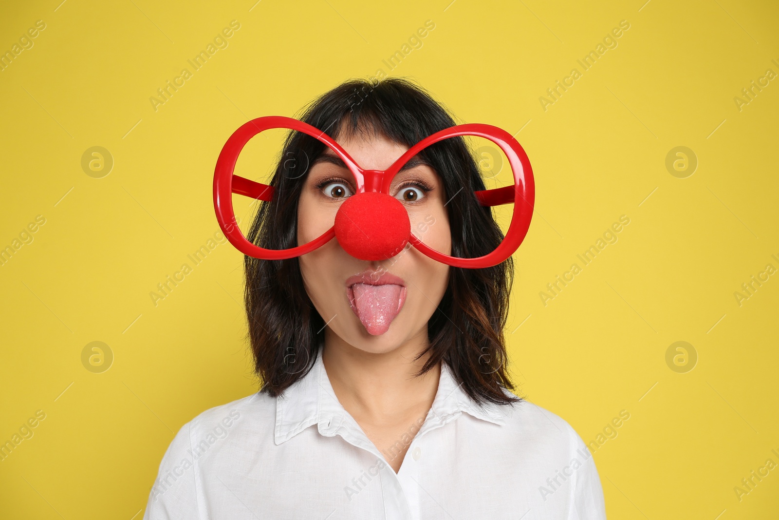 Photo of Funny woman with clown nose and large glasses on yellow background. April fool's day