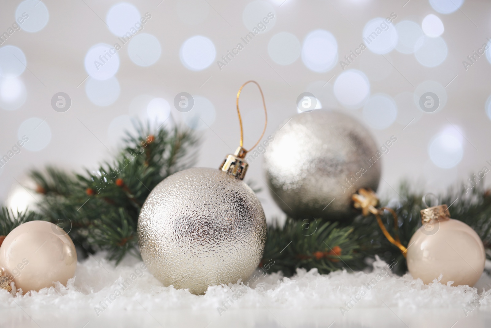 Photo of Beautiful Christmas balls and fir branches on snow against blurred festive lights