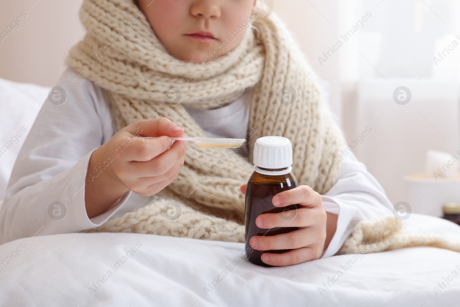 Photo of Sick girl taking cough syrup on bed at home, closeup. Cold medicine