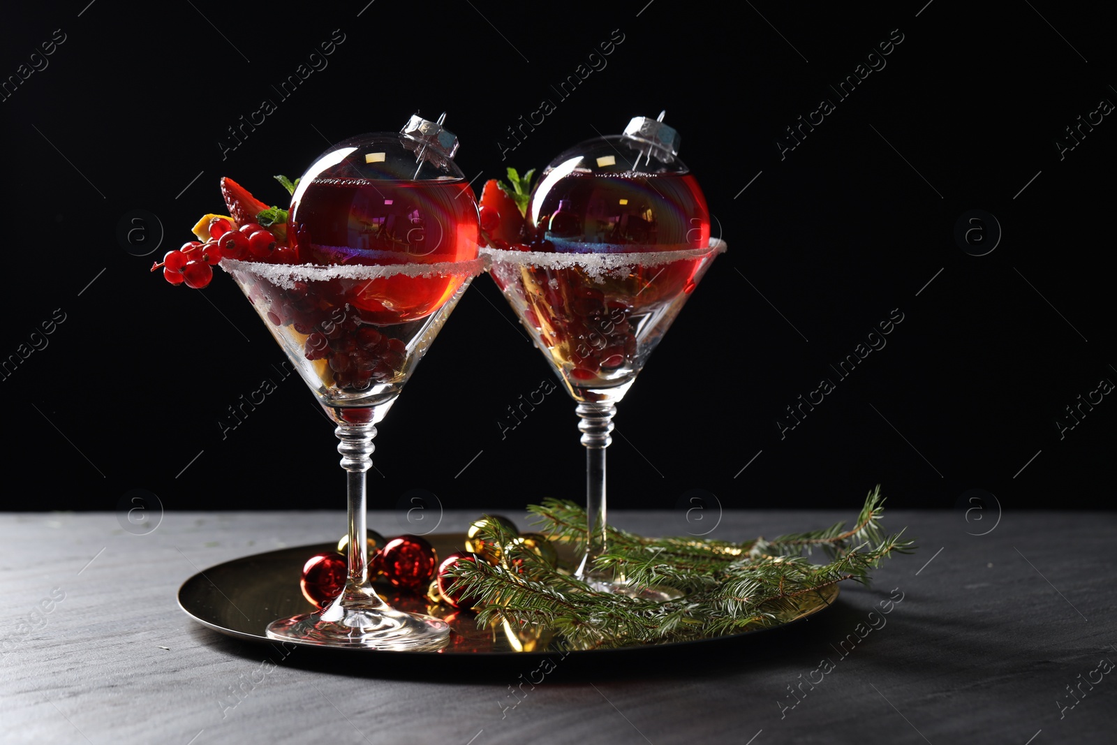 Photo of Creative presentation of Christmas Sangria cocktail in baubles and glasses on grey table against black background