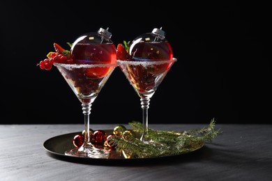 Photo of Creative presentation of Christmas Sangria cocktail in baubles and glasses on grey table against black background