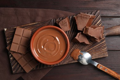 Photo of Tasty milk chocolate paste in bowl and pieces on table, top view