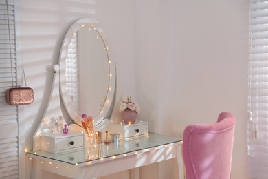 Elegant dressing table with lights and pink chair in stylish room interior