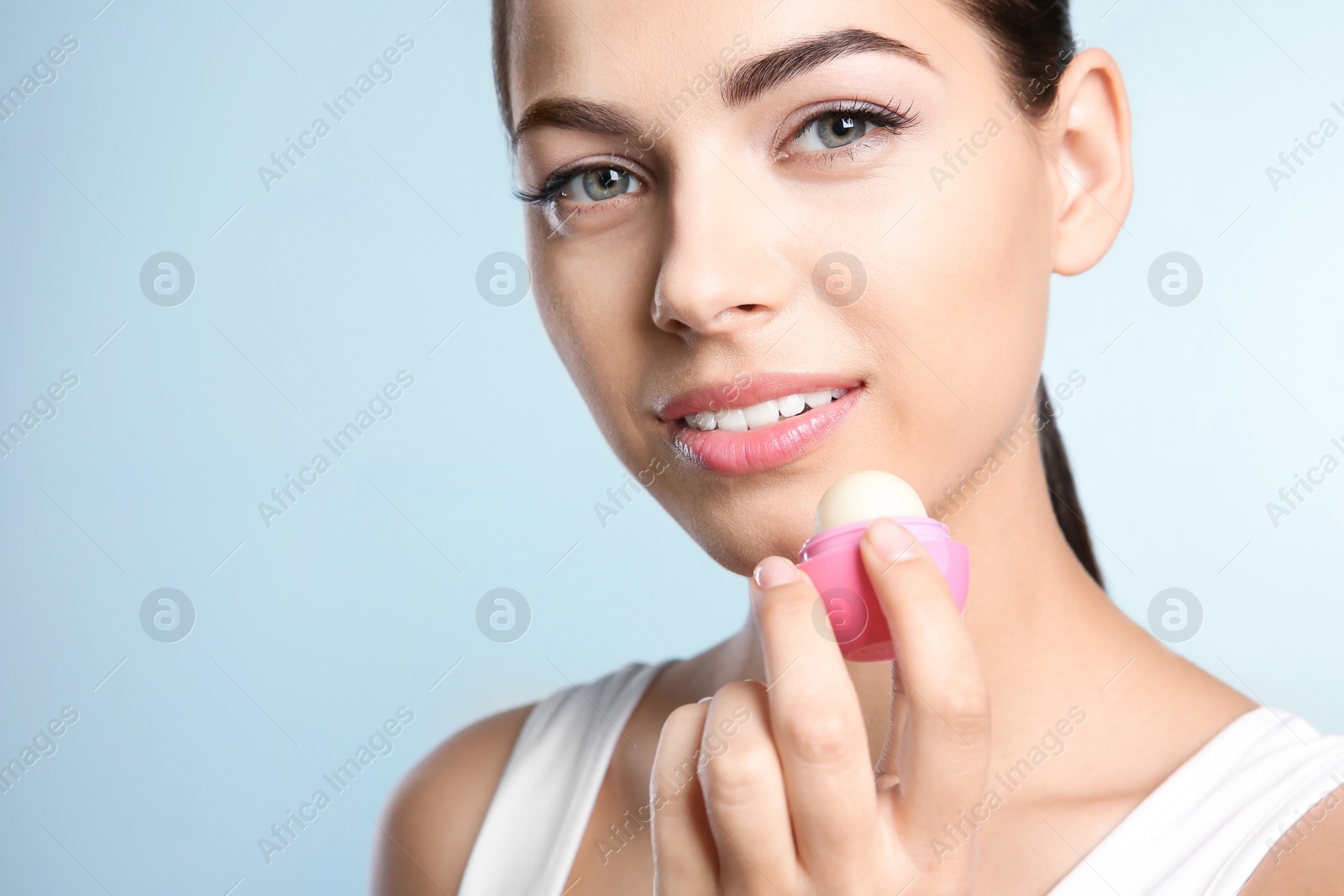 Photo of Young woman applying balm on her lips against color background