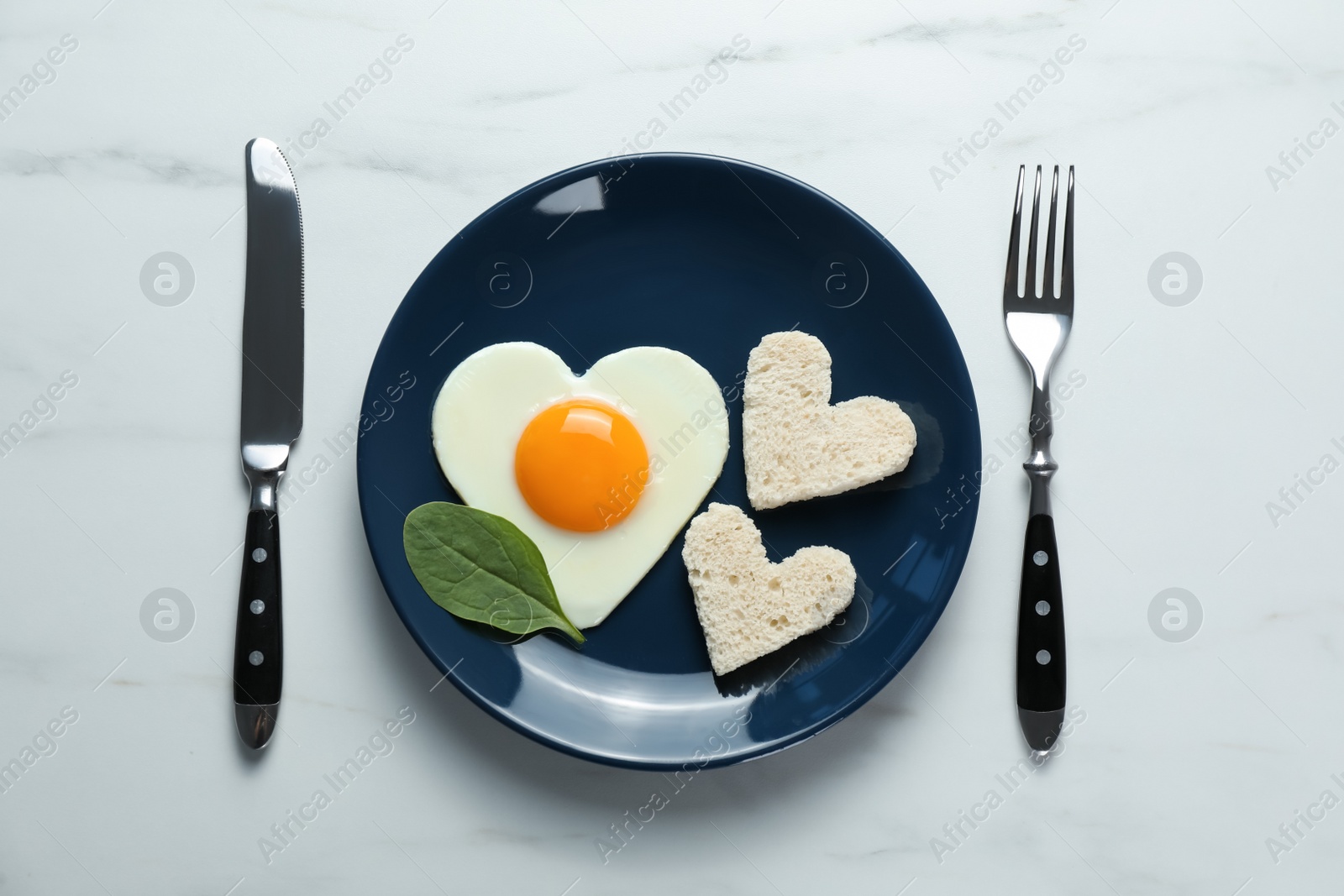 Photo of Romantic breakfast with heart shaped fried egg served on white marble table, flat lay